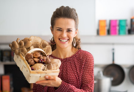 Portrait of smiling young housewife showing basket with mushroomsの写真素材
