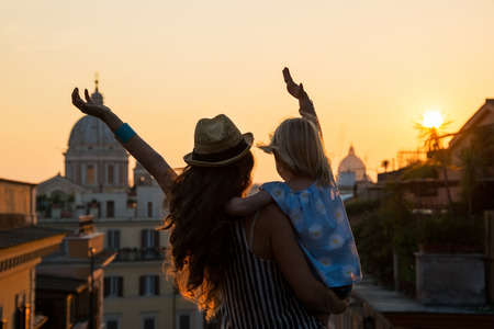 Silhouette of mother and baby girl looking on rooftops of rome on sunset and rejoicing. rear viewの写真素材