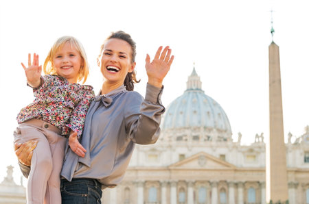 Portrait of happy mother and baby girl waving in front of basilica di san pietro in vatican city stateの写真素材