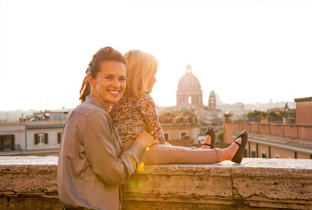 Mother and baby girl on street overlooking rooftops of rome on sunsetの写真素材