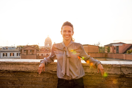 Portrait of happy young woman standing on street overlooking rooftops of rome on sunsetの写真素材