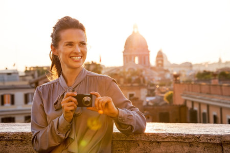 Happy young woman with photo camera on street overlooking rooftops of rome on sunset
