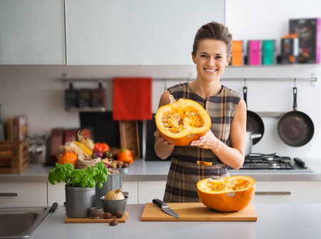 Portrait of happy young housewife in kitchen showing pumpkinの写真素材