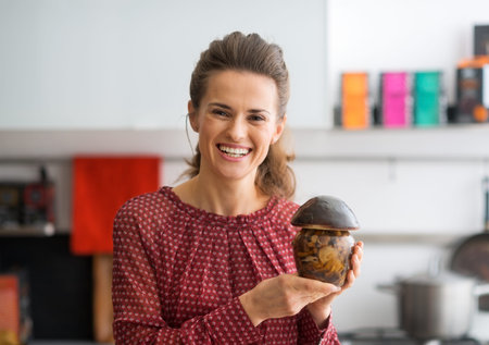 Portrait of happy young housewife showing jar of pickled mushroomsの写真素材