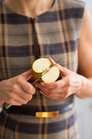 Closeup on young housewife cutting apple in kitchen