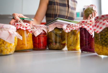 Closeup on jars of pickled vegetables and housewife writing in notepadの写真素材