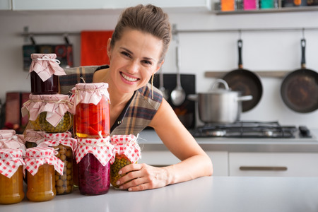 Portrait of happy young housewife looking out from jars with homemade fruits jam and pickled vegetablesの写真素材