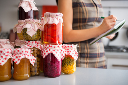 Closeup on jars with homemade fruits jam and pickled vegetables and housewife writing in notepad の写真素材