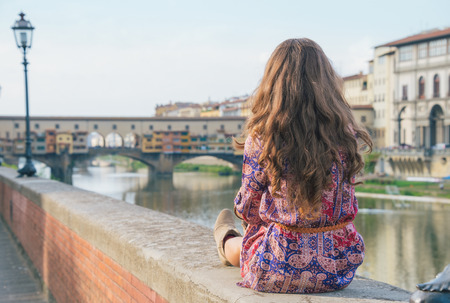 Young woman sitting near ponte vecchio in florence, italy. rear viewの写真素材