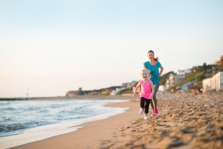 Healthy mother and baby girl running on beach in the eveningの写真素材