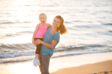 Portrait of healthy mother and baby girl on beach in the eveningの写真素材
