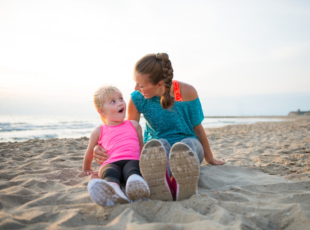 Portrait of fitness mother and surprised baby girl sitting on beachの写真素材