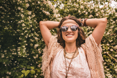 Longhaired hippy-looking young lady in knitted shawl and white blouse standing among flowersの写真素材