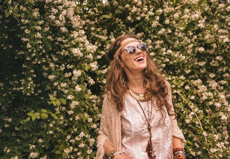 Longhaired hippy-looking young lady in knitted shawl and white blouse standing among flowers and looking up on copy spaceの写真素材