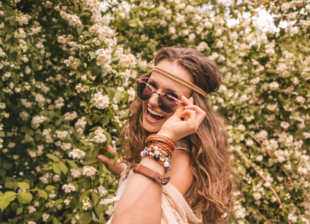 Longhaired hippy-looking young lady in knitted shawl and white blouse standing among flowersの写真素材