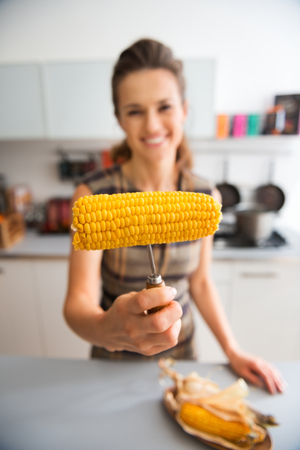 This one is for you... Perfectly cooked, just enough butter and salt, and bursting with flavor. An elegant woman smiles in her kitchen as she offers a corncob to her guest.の写真素材