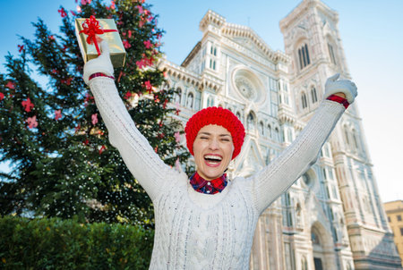Cheerful woman tourist with present gift box standing near large Christmas tree and enjoying holiday atmosphere in Florence, Italy. Christmas and travel concept.の写真素材