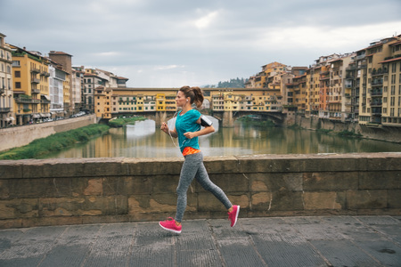 Young female jogger with headset is running by Arno riverside in Florence, Italyの写真素材