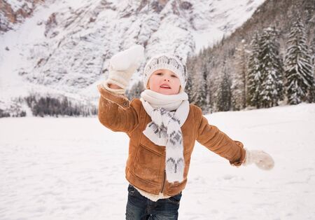 Winter leisure time spent outdoors among snowy peaks can turn the holidays into a fascinating journey. Child throwing snowball outdoors among snow-capped mountainsの写真素材
