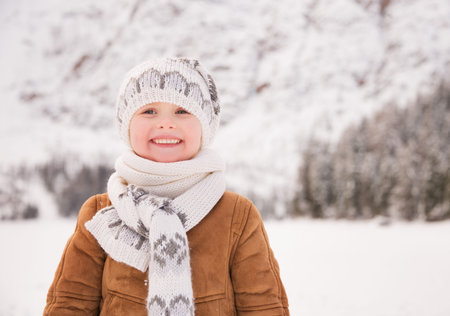 Winter leisure time spent outdoors among snowy peaks can turn the holidays into a fascinating journey. Portrait of smiling child standing outdoors among snow-capped mountainsの写真素材