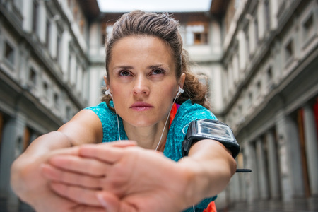 Now it is time to invest in your body and no matter you are at hometown or traveling. Close up on sporty young woman with earphones stretching in front of Uffizi gallery in Florence Italyの写真素材
