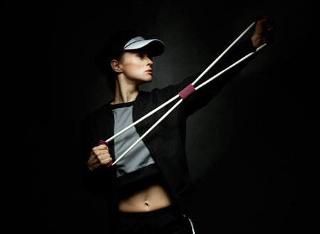 Boutique fitness studio style. Young fit woman training with resistance band against black backgroundの写真素材