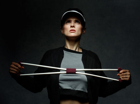 Boutique fitness studio style. Young fit woman training with resistance band against dark backgroundの写真素材