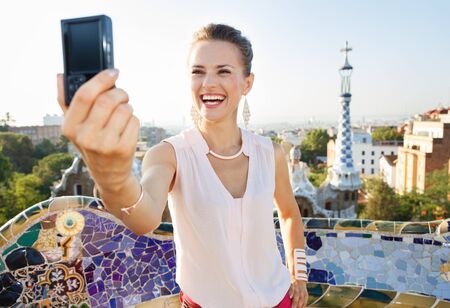 Refreshing promenade in unique Park Guell style in Barcelona, Spain. Happy young woman tourist taking selfie with digital photo camera in Park Guell, Barcelona, Spainの写真素材