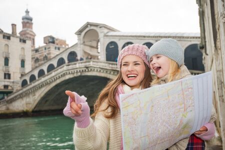 Modern family taking a winter break to enjoy inspirational adventure in Venice, Italy. Mother with map pointing daughter on something while standing in front of Ponte di Rialtoの写真素材