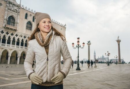 Delightful Venice, Italy can help make the most of your next winter getaway. Happy young woman tourist standing on St. Mark's Square near Dogi Palace and looking asideの写真素材