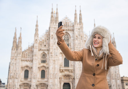 Discovering Italian treasures hidden in Milan. Smiling woman taking selfies with digital camera in the front of Duomo while sightseeing Milanの写真素材