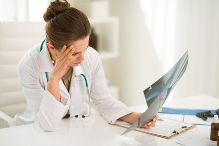 Modern health care. Concerned female doctor sitting at a desk in the office and looking on roentgenの写真素材