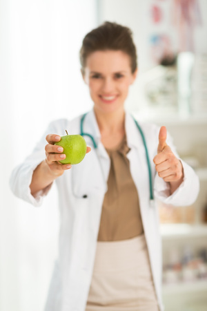 Modern health care. Closeup on female doctor giving green apple and showing thumbs upの写真素材