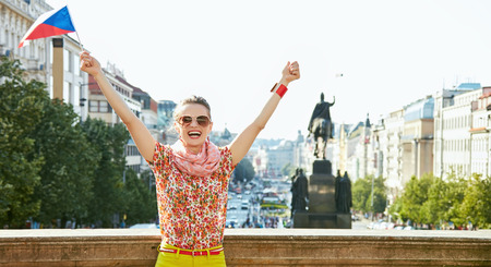 Catch the spirit of old Europe in Prague. Happy young woman in sunglasses with Czech flag standing near National Museum at Wenceslas Square and rejoicingの写真素材