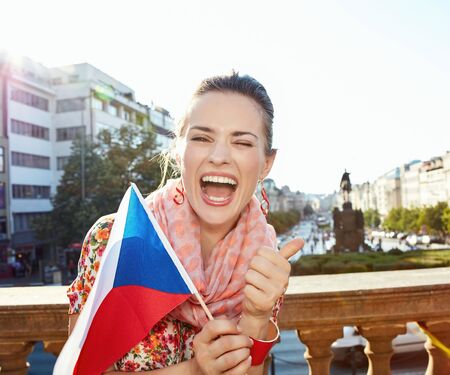Catch the spirit of old Europe in Prague. Portrait of happy young woman with Czech flag showing thumbs up while standing near National Museum at Wenceslas Squareの写真素材