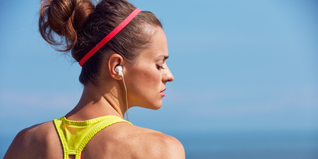 Look Good, Feel great! Portrait of young healthy woman in fitness outfit listening to the music at the embankmentの写真素材