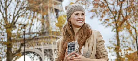 Autumn getaways in Paris. smiling young tourist woman near Eiffel tower with cellphone looking asideの写真素材