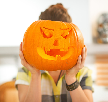 Frightful Treats on the way. Portrait of housewife in the Halloween decorated kitchen holding a big orange pumpkin Jack-O-Lantern in front of headの写真素材