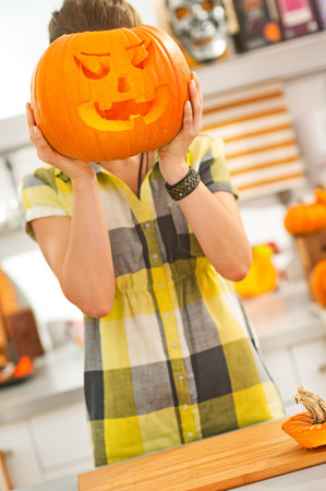 Frightful Treats on the way. young woman in the Halloween decorated kitchen holding a big orange pumpkin Jack-O-Lantern in front of headの写真素材