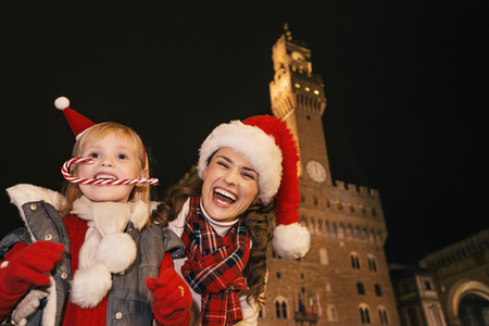 Trip full of inspiration at Christmas time in Florence. Portrait of happy young mother and child tourists in Christmas hats in the front of Palazzo Vecchio in Florence, Italy with Christmas candy caneの写真素材