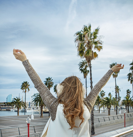 in Barcelona for a perfect winter. Seen from behind young tourist woman in earmuffs on embankment in Barcelona, Spain rejoicingの写真素材