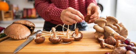 A woman's elegant hands are working on stringing mushrooms together as she prepares a fall meal. Soon, the rich, earthy aroma of roasted vegetables and fall fruits will fill the air.の写真素材