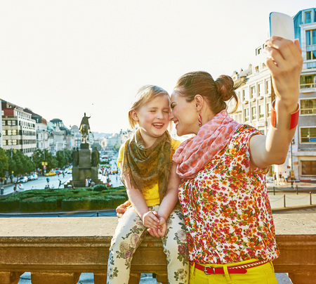The spirit of old Europe in Prague. smiling young mother and child tourists on Vaclavske namesti in Prague, Czech Republic with phone taking selfieの写真素材