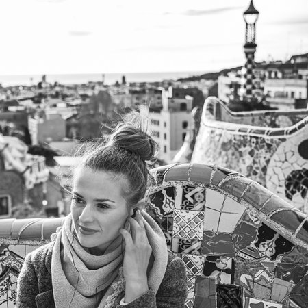 Barcelona signature style. young tourist woman in coat in Barcelona, Spain listening audioguide while sitting on benchの写真素材