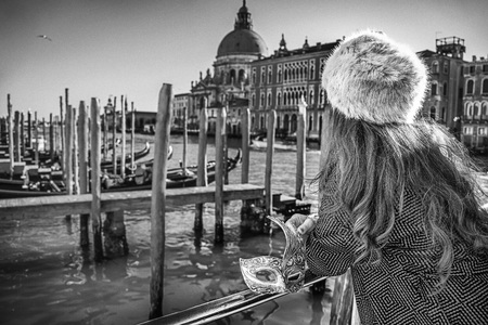 Another world vacation. Venetian mask in hand of woman in fur hat in Venice, Italy. Seen from behindの写真素材