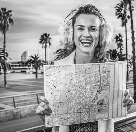 in Barcelona for a perfect winter. smiling modern woman in earmuffs on embankment in Barcelona, Spain with mapの写真素材
