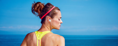 Look Good, Feel great! Seen from behind Relaxed young woman in fitness outfit listening to the music at the embankmentの写真素材
