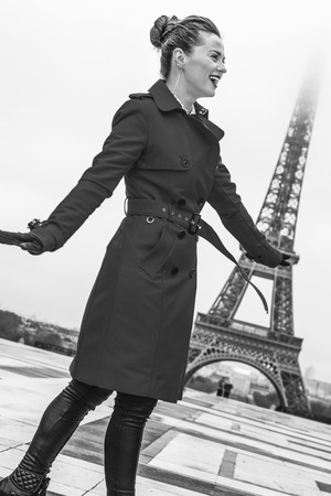 Bright in Paris. Full length portrait of smiling trendy woman in red trench coat in the front of Eiffel tower in Paris, Franceの写真素材