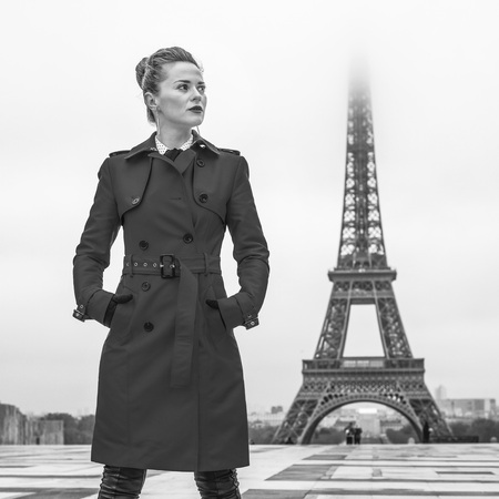Bright in Paris. Full length portrait of young woman in red trench coat against Eiffel tower in Paris, France looking asideの写真素材