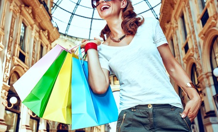Discover most unexpected trends in Milan. Smiling fashion woman in eyeglasses with colorful shopping bags in Galleria Vittorio Emanuele II looking into the distanceの写真素材
